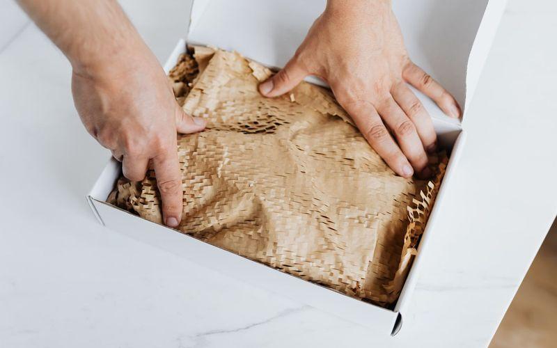 Mãos embalando um pedido em caixa de papelão